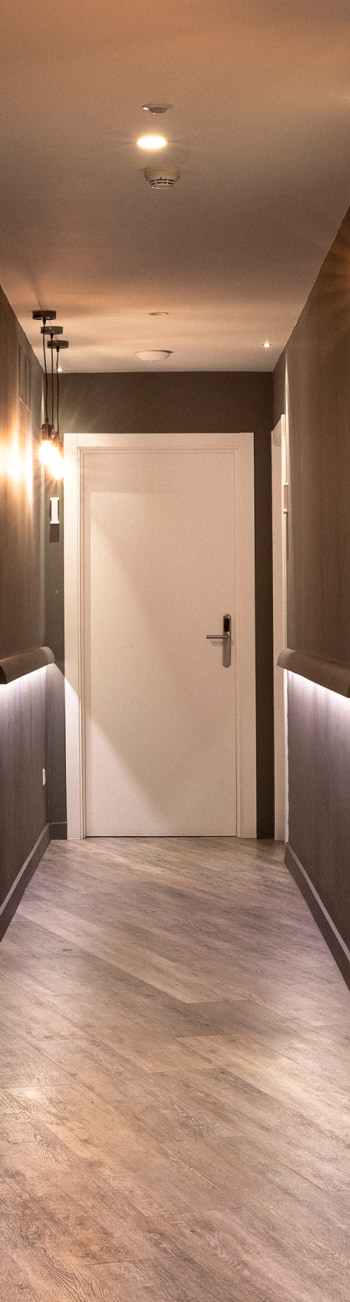 Korytarz hotelowy Korytarz hotelowy - Oświetlony korytarz hotelowy z drzwiami i drewnianą podłogą